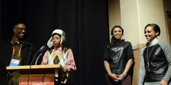 A young speaker at a podium with other event participants