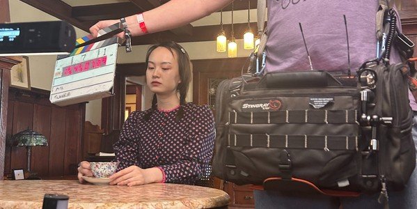 A production slate held before a scene with an actor and camera equipment